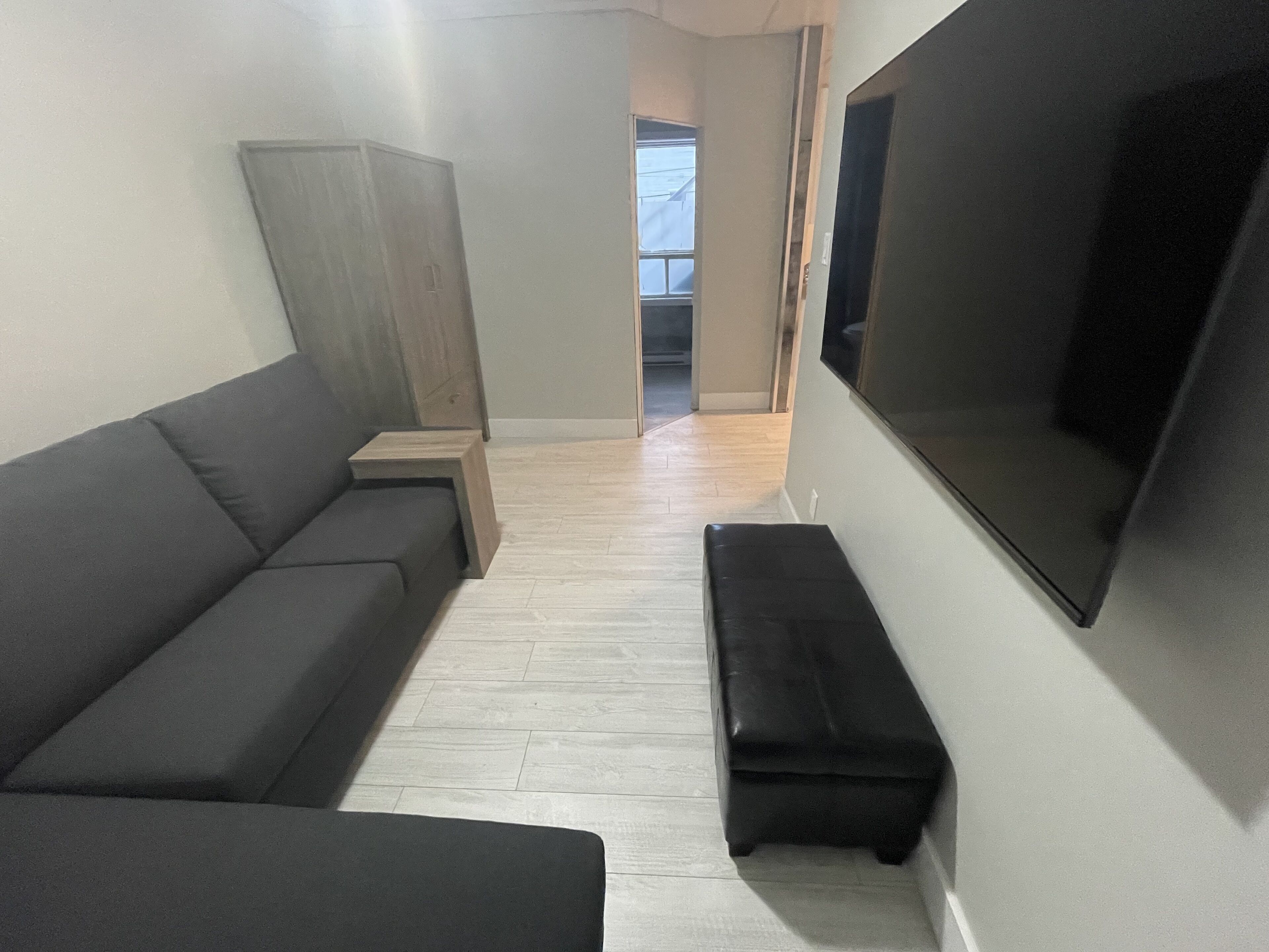 Una sala de estar con un sofá, un banco, un televisor y un aparador de madera.
