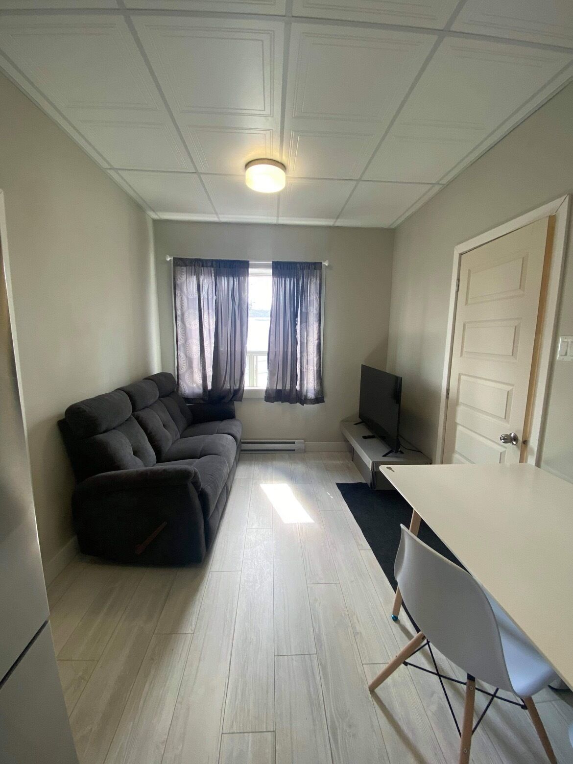 A room with a sectional sofa, a TV, a dining table with chairs, and a window with curtains.