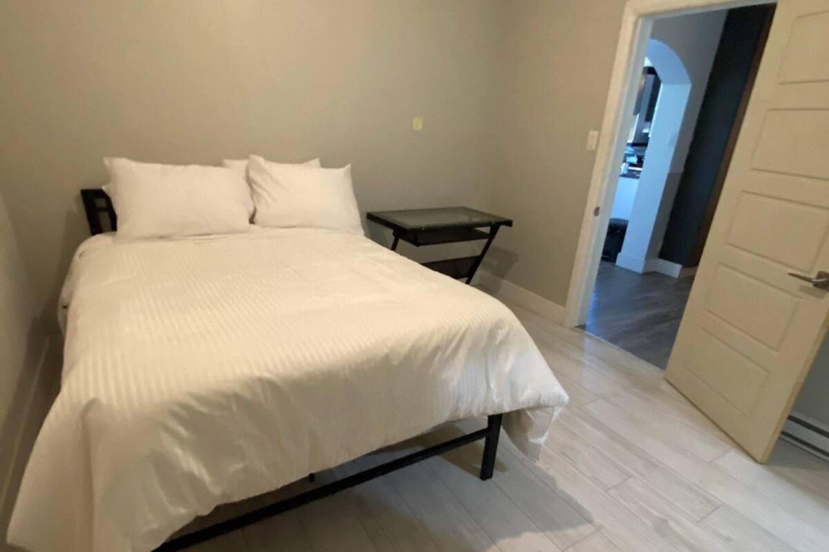 A bedroom with a bed, a bedside table, and a door leading to another room.