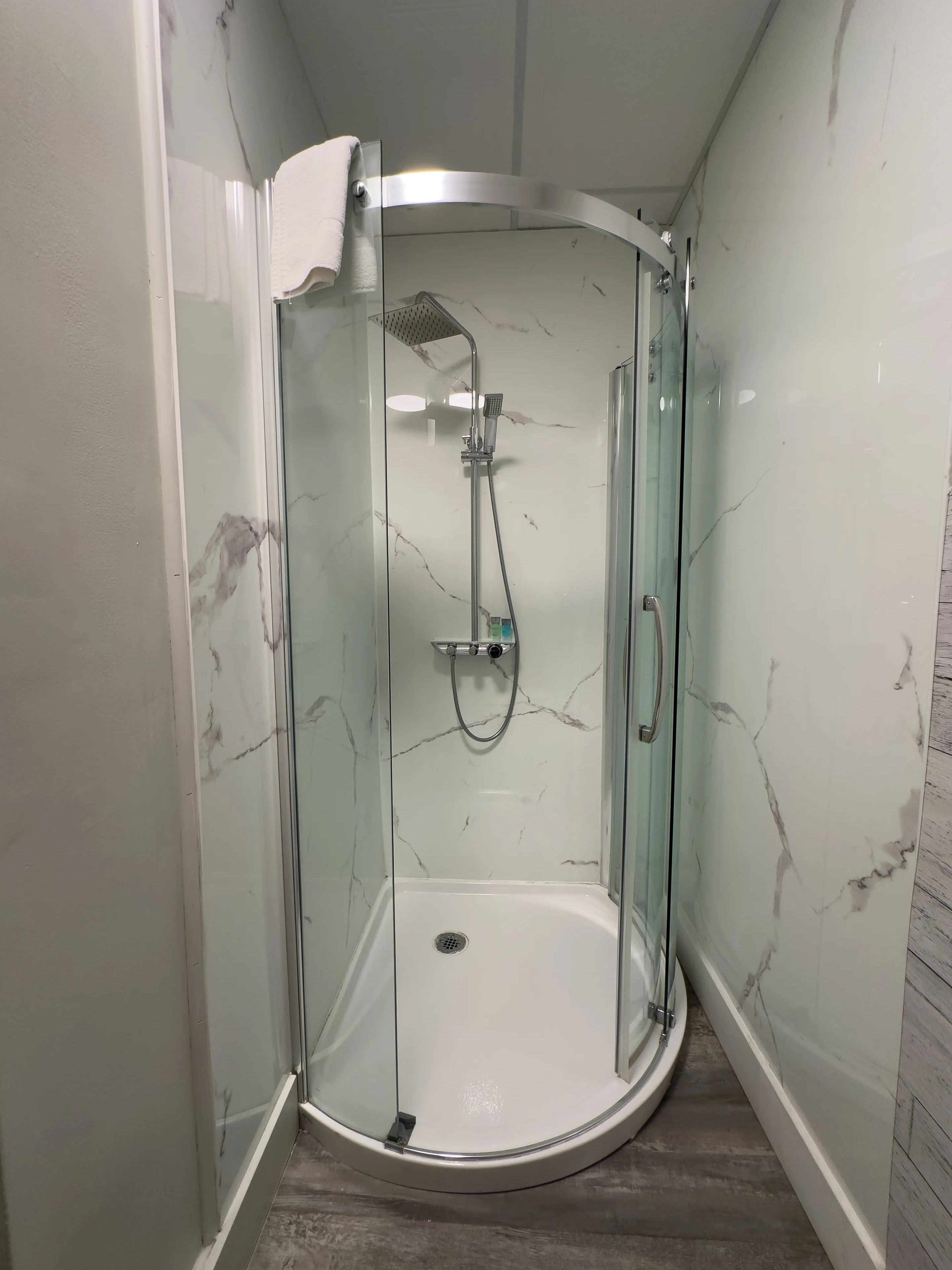 A glass-enclosed shower with a handheld showerhead and a wall-mounted faucet.