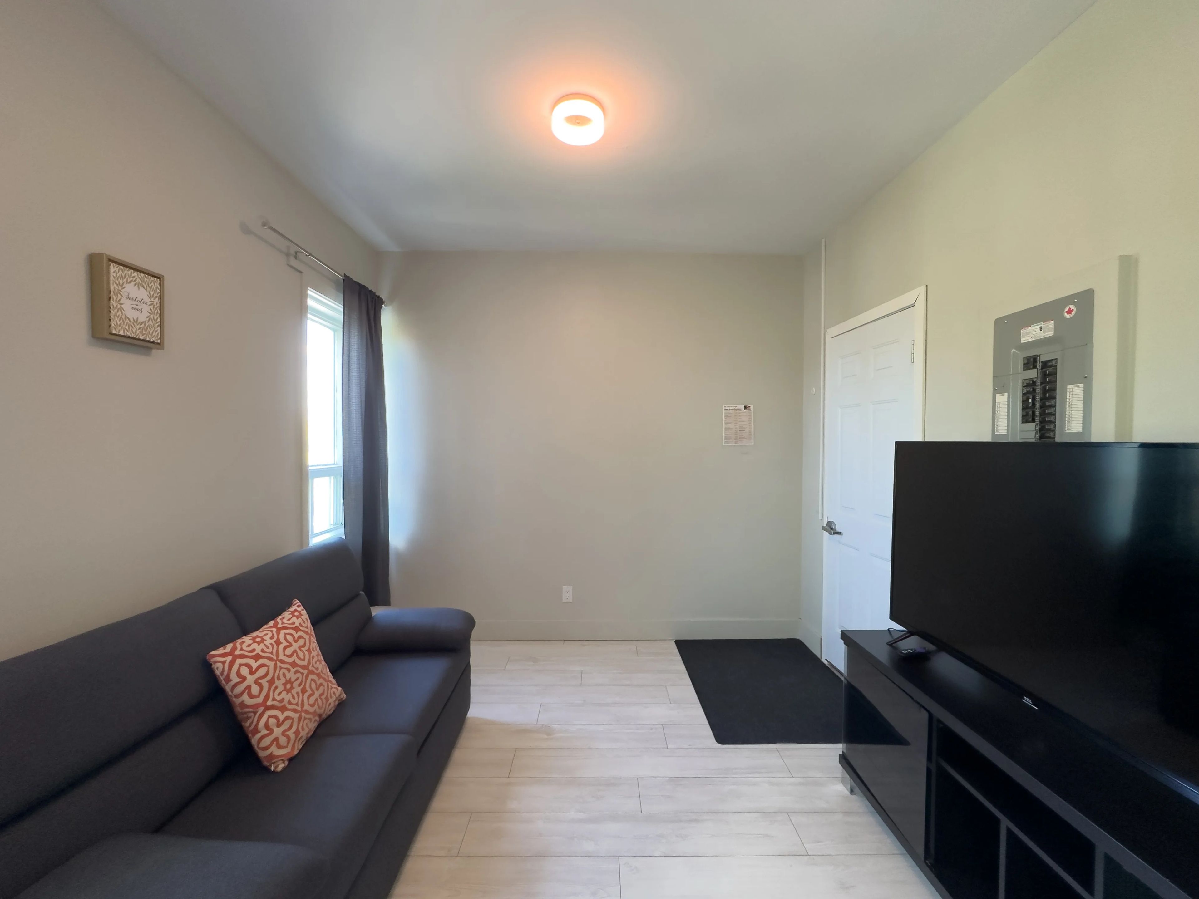 A living room with a dark sofa, a flat-screen TV, a light-colored floor, and a white door.