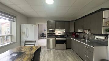 A modern kitchen with stainless steel appliances, a dining area with a wooden table, and a view through a window.