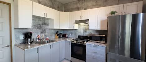 A modern kitchen with white cabinets, a stainless steel refrigerator, a gas stove, and a microwave.