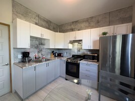 A modern kitchen with white cabinets, a stainless steel refrigerator, a gas stove, and a microwave.