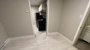 A narrow hallway with light-colored wooden flooring and white walls. - Le Convivial (Rouyn-Noranda)