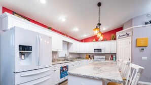 A modern kitchen with white cabinetry, a granite countertop, and a stainless steel refrigerator. - 3/2 updated pool home that sleeps 8 about 5 minutes from WEC (Ocala)