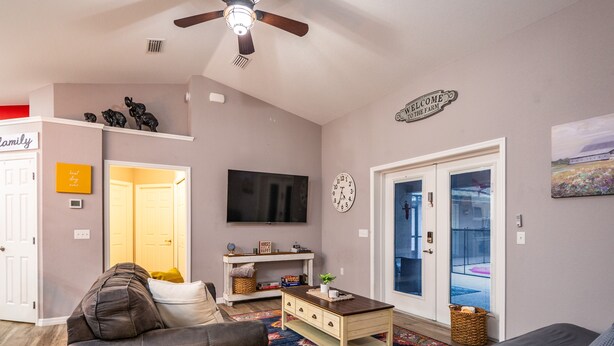 A living room with a sofa, a coffee table, a TV, and a door leading to a balcony. - 3/2 updated pool home that sleeps 8 about 5 minutes from WEC (Ocala)