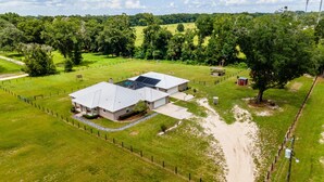 An aerial view of a large, single-story building with a flat roof, surrounded by a fenced property with green grass and trees. - 3/2 updated pool home that sleeps 8 about 5 minutes from WEC (Ocala)