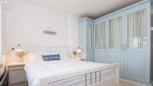 Une chambre avec un lit blanc, une table de chevet avec une lampe, un tableau accroché au mur et des armoires bleu clair.