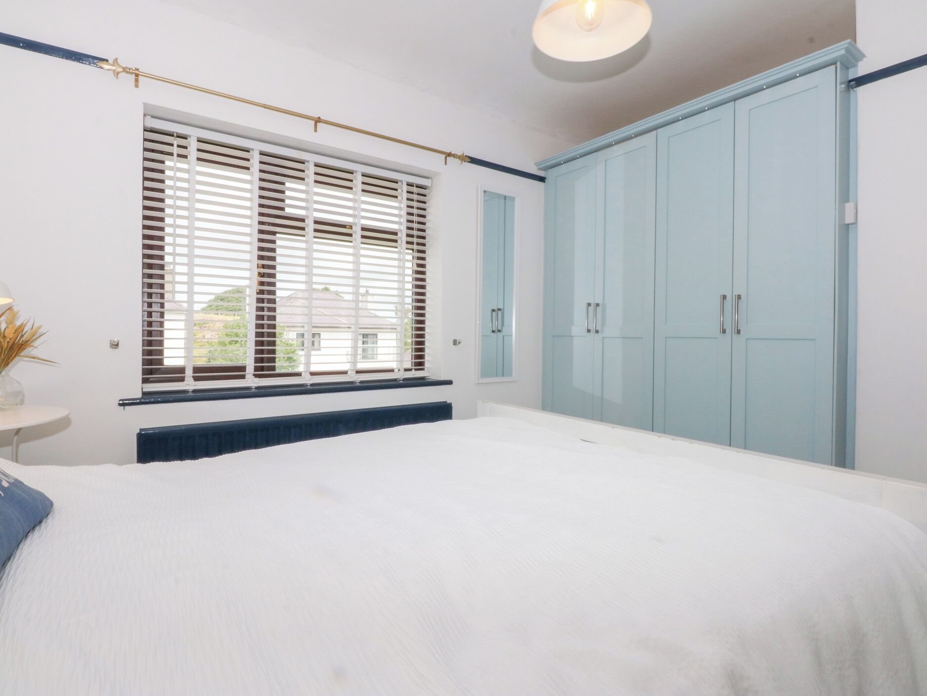 Une chambre avec un grand lit, une fenêtre avec des stores, un radiateur et des armoires bleu clair.