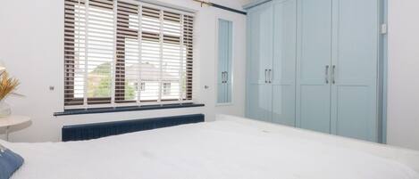 Une chambre avec un grand lit, une fenêtre avec des stores, un radiateur et des armoires bleu clair.