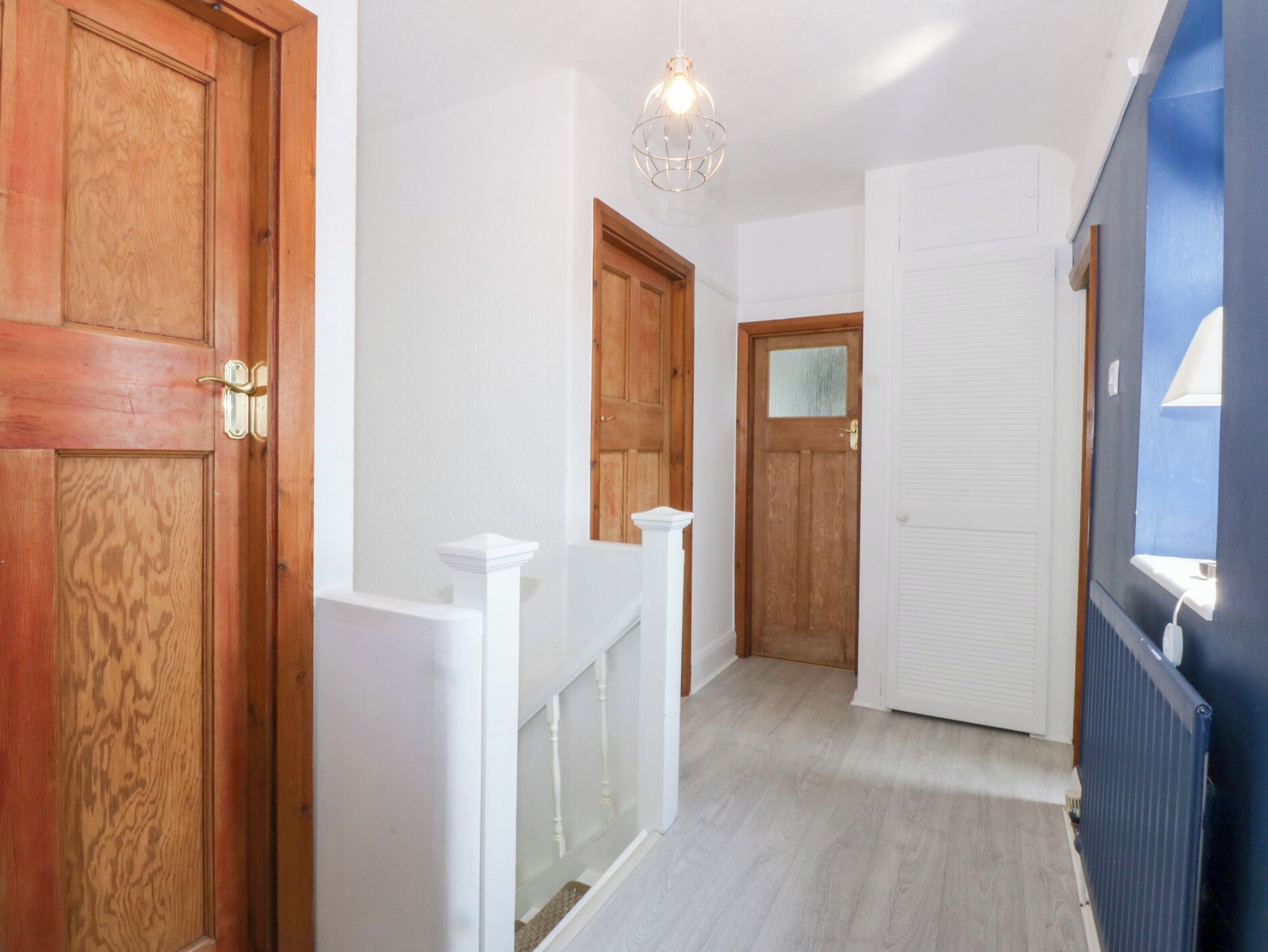 Un couloir avec des portes en bois, une rambarde blanche et un mur bleu avec un radiateur.