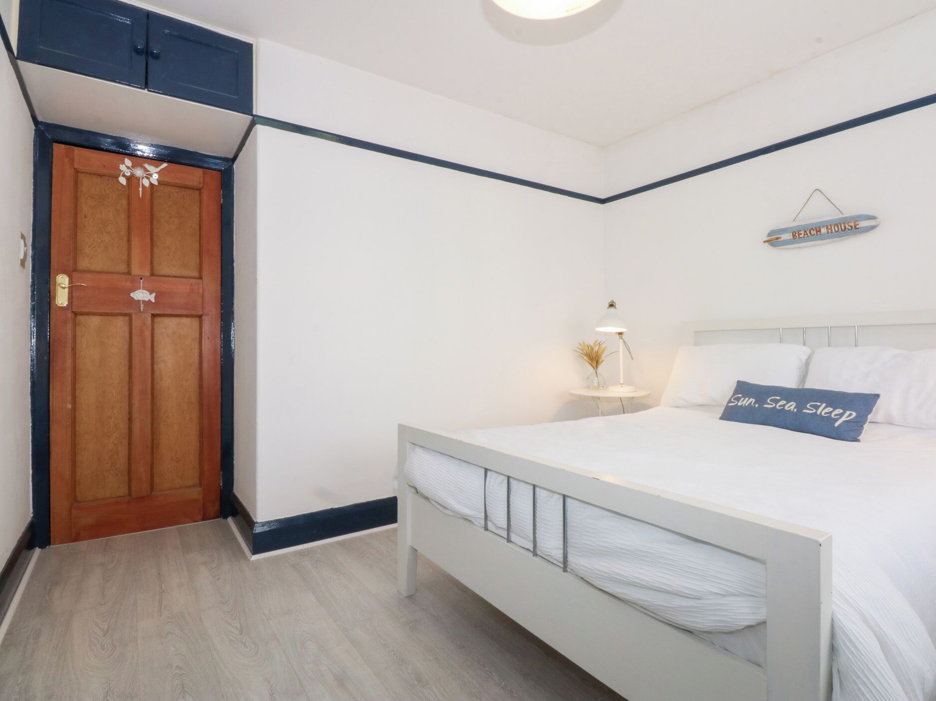 Un dormitorio con cama, mesita de noche, lámpara, un letrero en la pared y una puerta.