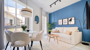 Una sala de estar moderna con un sofá blanco, sillas color beige, una mesa de centro y un amplio ventanal con cortinas.