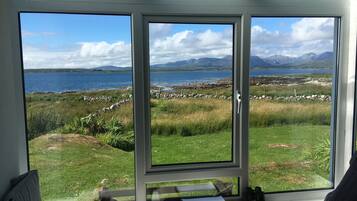A room with a large window offering a view of a grassy landscape, a body of water, and distant mountains.