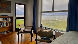 A room with a large window offering a view of a landscape, a bookshelf, a chair, and a bed.