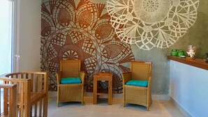 Ein Zimmer mit Korbmöbelstühlen und einem Tisch, eine Wand mit aufwendigen Mustern und einer Deckenleuchte.