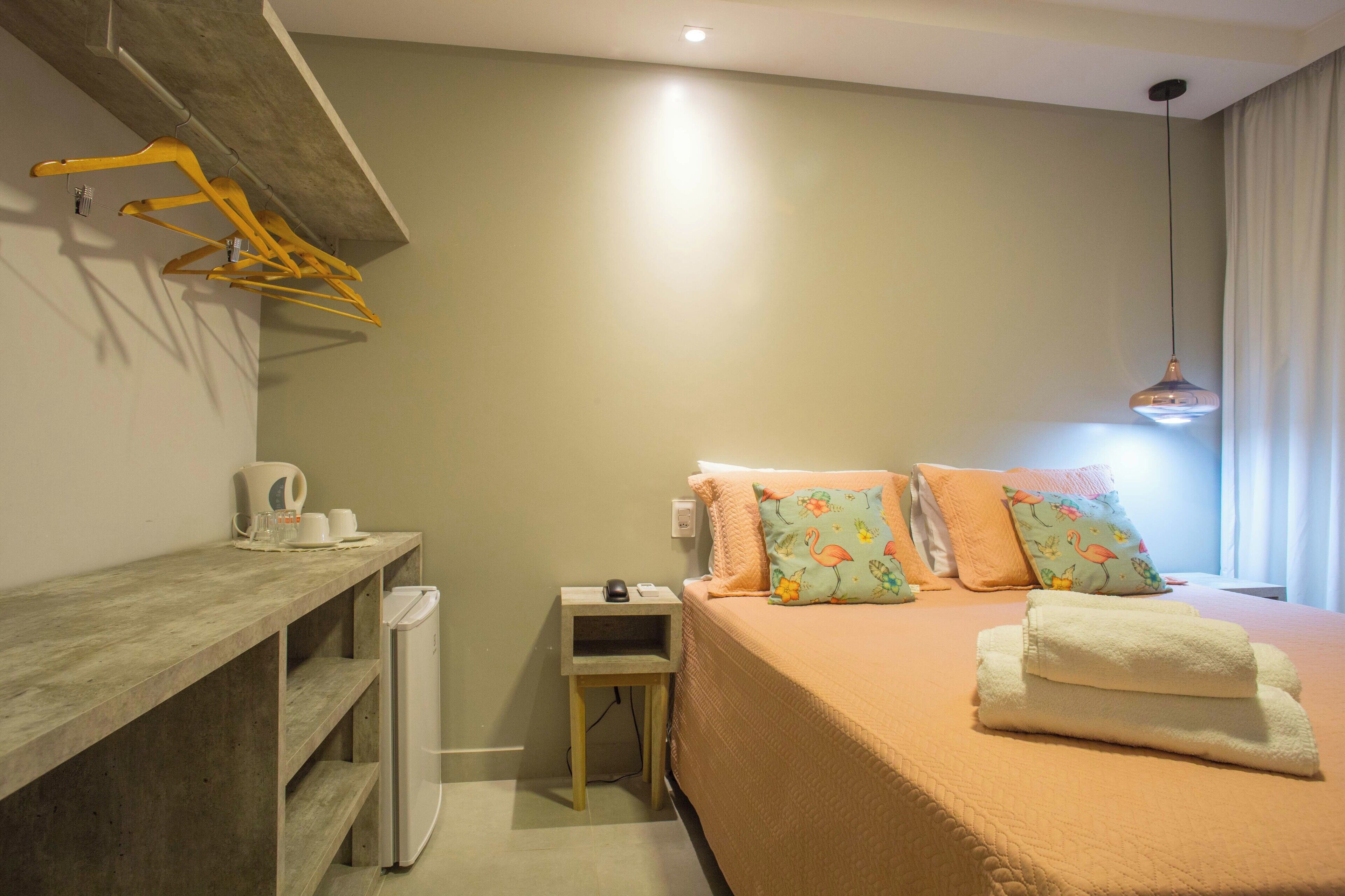 A bedroom with a bed, a bedside table, a small desk, a heater, and a hanging light fixture.
