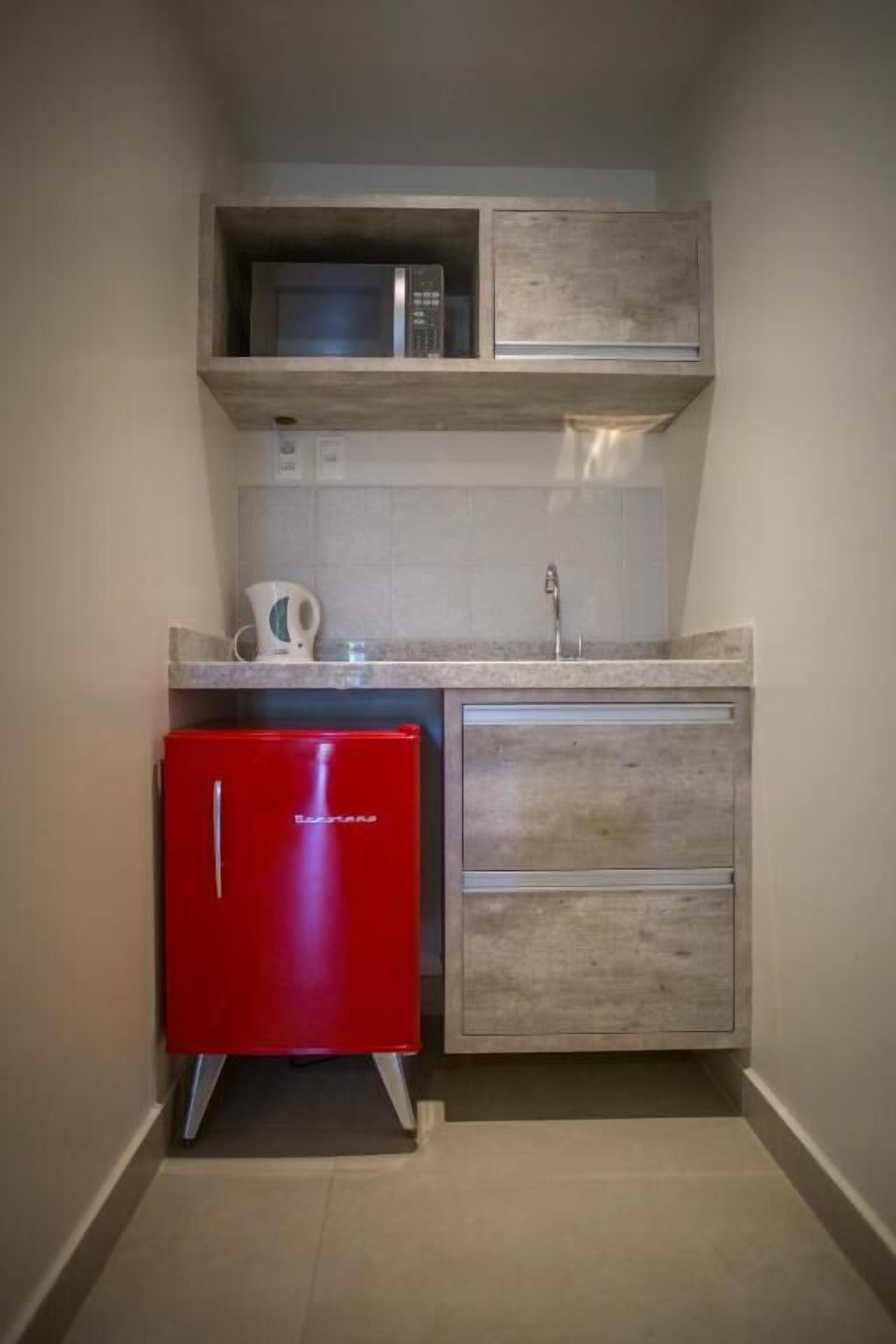 A compact kitchen with a microwave, a red refrigerator, and a sink.