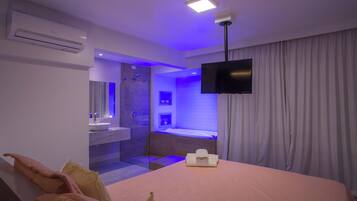 A hotel room with a bed, a TV, an air conditioner, a bathroom with a bathtub, and a shower.