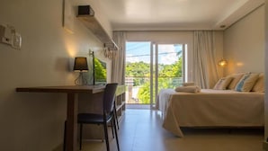 Ein Hotelzimmer mit Bett, Schreibtisch mit Stuhl, Fernseher und Balkon mit Blick auf Grünflächen.