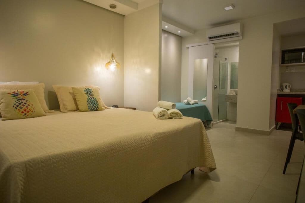 Habitación de hotel con una cama grande, un escritorio, una silla y un baño visible a través de una puerta abierta.
