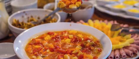 Un tazón de sopa de verduras con una cucharada siendo levantada, rodeado de diferentes alimentos sobre una mesa.