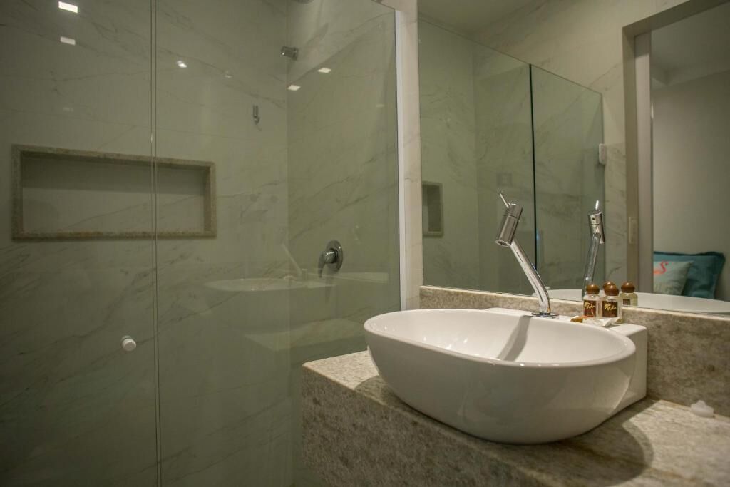 A modern bathroom with a large white sink, a glass shower enclosure, and a marble countertop.