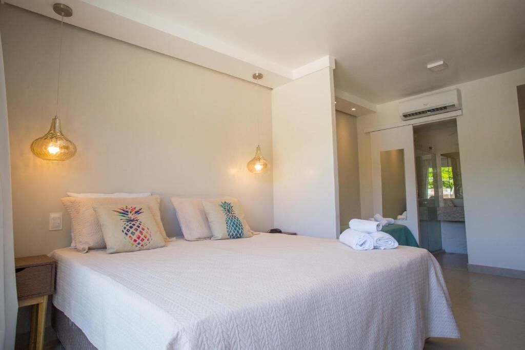 Quarto com cama, duas luminárias na parede, mesa de cabeceira e ar condicionado visível.