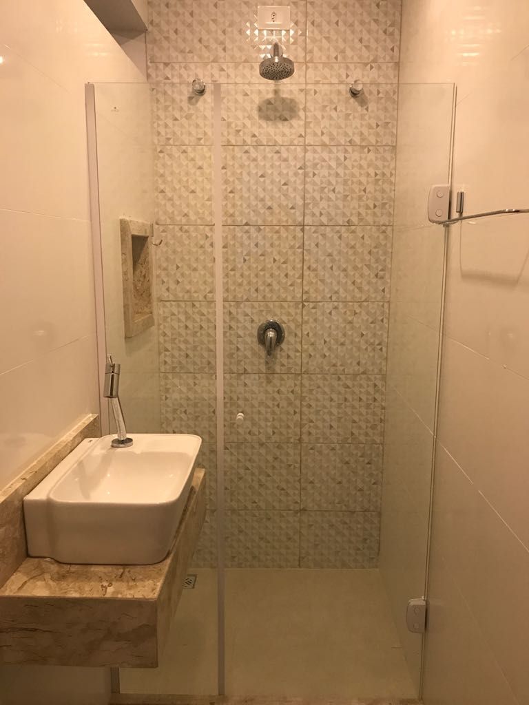 Eine Dusche mit Glastür, ein Waschbecken mit Marmorplatte und eine geflieste Wand mit geometrischem Muster.