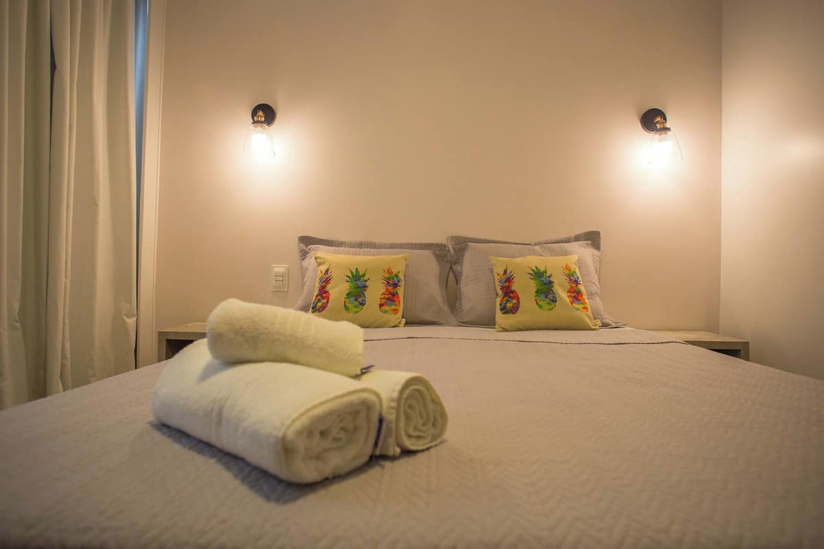A neatly made bed with two pillows, a rolled towel, and two wall-mounted lights.