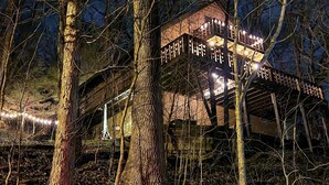 Ein Baumhaus mit Holzterrasse und Geländern, umgeben von Bäumen.