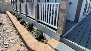 A covered porch with white railings, a stone pathway, and a flower bed. - Elephant Lake Resort Oasis New (Elephant Butte)