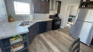 A modern kitchen with dark cabinets, a stainless steel refrigerator, and a wooden floor. - Elephant Lake Resort Oasis New (Elephant Butte)