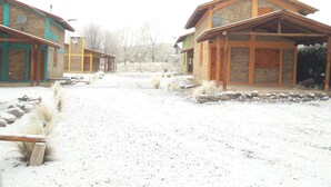 A rustic building with a wooden facade and a stone foundation, surrounded by a gravel path and sparse vegetation. - Cabin Arroyo de Uco - Between mountains, streams and wineries (Manzano Historico)