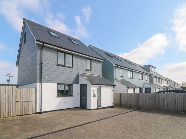 Une rangée de maisons modernes à deux étages, avec un revêtement extérieur gris et blanc, une clôture en bois et une allée pavée.