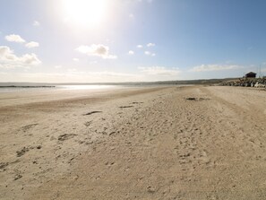 Une vaste plage de sable, parsemée d’empreintes, et une petite construction sur la droite.