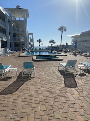 A pool area with lounge chairs and a view of the ocean.