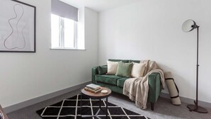 A modern living room with a green sofa, a round coffee table, a floor lamp, and a framed abstract artwork on the wall. - Stylish 1BR Apt, Hunslet Leeds City Centre (Leeds)