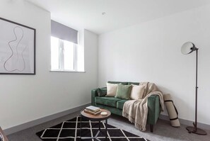 Een moderne woonkamer met een groene bank, een ronde salontafel, een vloerlamp en een abstract kunstwerk in een lijst aan de muur.