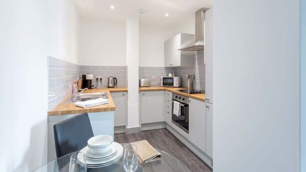 A compact kitchen with white cabinets, a microwave, a stove, and a sink. - Stylish 1BR Apt, Hunslet Leeds City Centre (Leeds)
