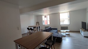 A spacious living area with a wooden dining table, black chairs, a grey sofa, and a small white table.