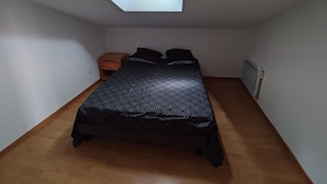 A small, single-bed room with a skylight, wooden floor, and a nightstand.