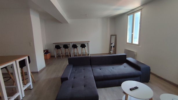 A modern living room with a sectional sofa, a small table, and a dining area with chairs.