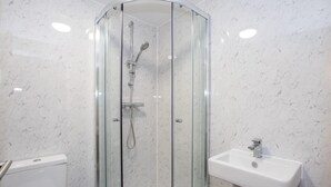 Un baño con ducha de vidrio, lavamanos blanco y un inodoro.