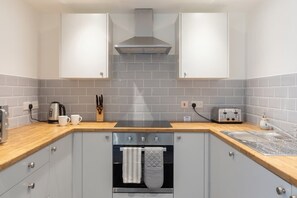 A kitchen with grey cabinets, a stainless steel range hood, a built-in oven, a toaster, and a sink.