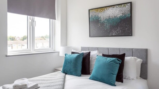 Una habitación de hotel con cama, almohadas, una ventana y un cuadro en la pared.