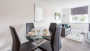 Un área de comedor moderna con una mesa de vidrio, sillas negras y un sofá gris al fondo.