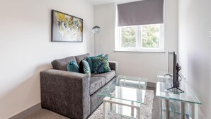 Un salón moderno con un sofá gris, una mesa de centro de vidrio y un cuadro en la pared.