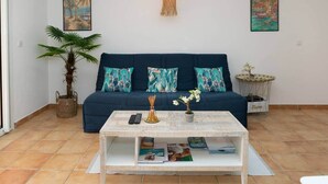 A living room with a dark blue sofa, patterned cushions, a coffee table with magazines, a potted plant, and wall art. - Blue Bay Apartment, Orient Bay, near the beach (Collectivité de Saint-Martin)